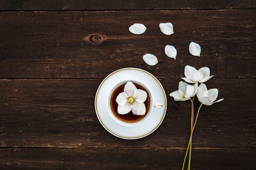 A cup with tea, white flowers of anemones on a wooden background. View from above.