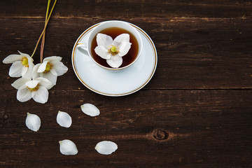 A cup with tea, white flowers of anemones on a wooden background. View from above.