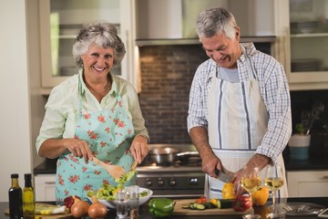 Portrait of senior woman with man preparing food in kitchen
