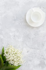 Lily of the valley bouquet and empty cup for coffee on a concret