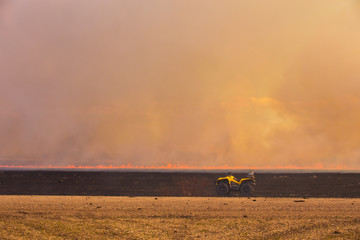 An ATV parked on the edge of a burning agriculture field with a wall of smoke in the background