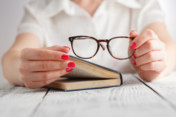 woman reading a book and in her hand she holds a pair of eyeglasses