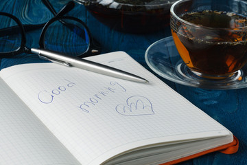Cup of tea with notebook and glasses on wooden table