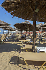 Beautiful Ionian sandy resort beach in Greece with sunbeds and straw sunshades, umbrellas. Vacation destination. Public beach