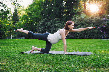 Fototapeta premium Beautiful pregnant woman doing prenatal yoga on nature outdoors.