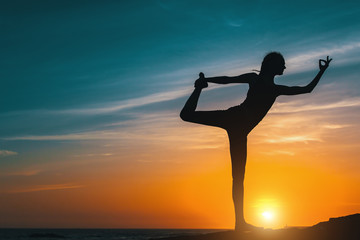 Silhouette young woman, exercise on the beach at amazing sunset. Yoga and Health lifestyle.