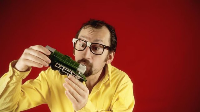 A funny adult man reliving his childhood, playing with a model train, carefree and happy.
