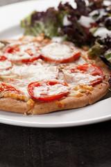  
Homemade pizza with marinara sauce topped with parmesan cheese and sliced tomatoes with a side salad macro shot
