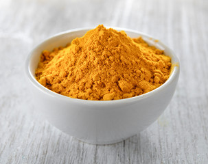 Turmeric powder in white cup on wooden floor