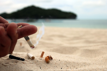 Hand smoking cigarette and ashtray on the beach.  