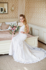 Pretty young Bride. Blonde-haired woman with wedding hair-style with a long tail. Boudoir morning of the bride. Looking on her bouquet