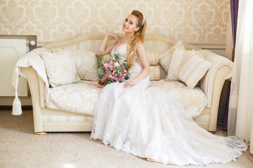 Obraz na płótnie Canvas Pretty young Bride. Blonde-haired woman with wedding hair-style with a long tail. Boudoir morning of the bride. Looking on her bouquet