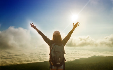 Freedom traveler woman standing with raised arms and enjoying a beautiful nature and cheering young woman backpacker at sunrise seaside mountain peak