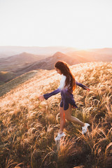 Happy young woman running on feather grass field in sunset light. Nature lifestyle and amazing view around. Long black hair with colored locks