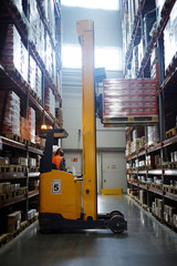 Loader lifting packed goods on shelf of storehouse