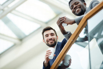 Portrait of handsome bearded businessman with African-American colleague looking down from glass...