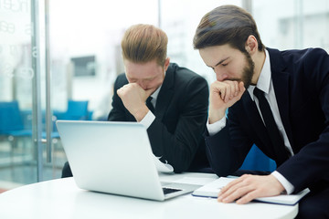 Stressed businessmen sitting by workplace in front of laptop