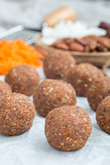 Obraz na płótnie Canvas Healthy paleo energy balls with carrot, nuts, dates and coconut flakes, on parchment, vertical