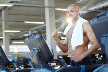 Fototapeta na wymiar Shirtless man with towel exercising on treadmill in gym