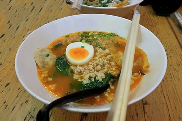 Spicy Tom Yum noodles soup with pork and egg in white a bowl. Selective focus and shallow depth of field.