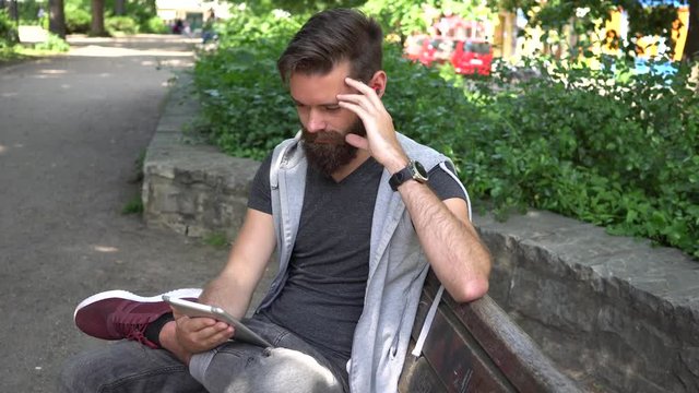 Cute guy with beard and earphones watching videos on a digitale e-reader tablet
