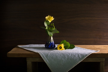 Beautiful yellow flowers with green leaf in the ceramics vase and fall out the vase  put on the plank in dim light room