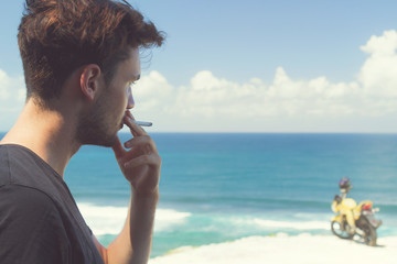 Handsome young man relaxing and smoking cigar on the beach. 