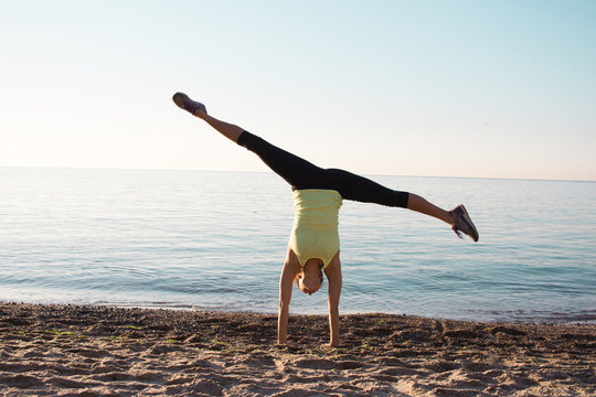 young professional gymnast woman dance on the beach,  training  exercises standing on hands, sunrise in sea or ocean background 