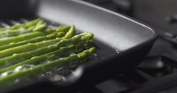 Slide shot of cooking frozen green asparagus on grill pan, 4k prores footage