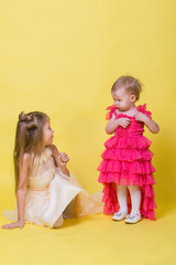 Fototapeta na wymiar Two sisters in dresses on a yellow background in the Studio