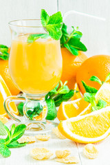 Orange juice in a glass on a white wooden table with whole and sliced oranges
