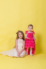 Fototapeta na wymiar Two sisters in dresses on a yellow background in the Studio