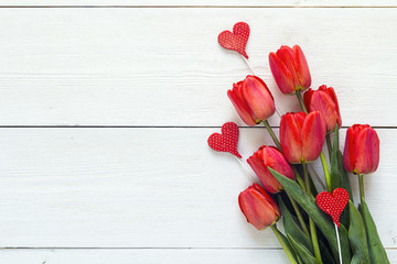 Background with bouquet of red tulips and decorative hearts on white wooden boards.