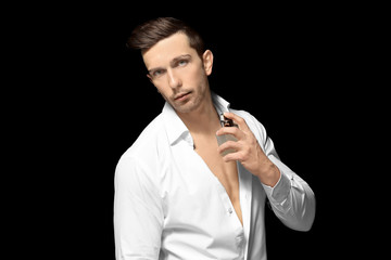 Handsome man using perfume on black background