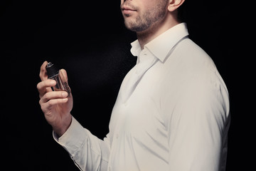 Handsome man using perfume on black background
