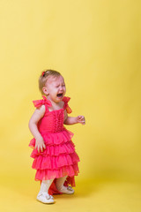 Little girl in pink dress crying on a yellow background