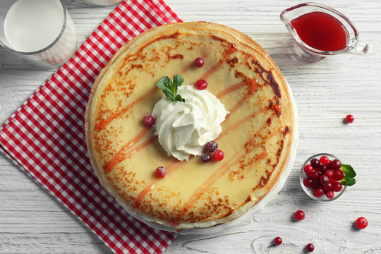 Tasty pancakes with cream and berries on table