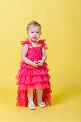 Girl toddler in a pink dress on a yellow background in the Studio