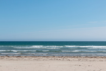 Fototapeta na wymiar Empty beach with white sand, deep blue water and blue sky
