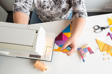 needlework and hand quilting in the workshop of a tailor woman on white background - close up on hands with a sewing machine at the table and thread, fabrics, needles, pins, buttons, scissors