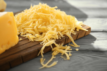 Wooden board with grated cheese on table