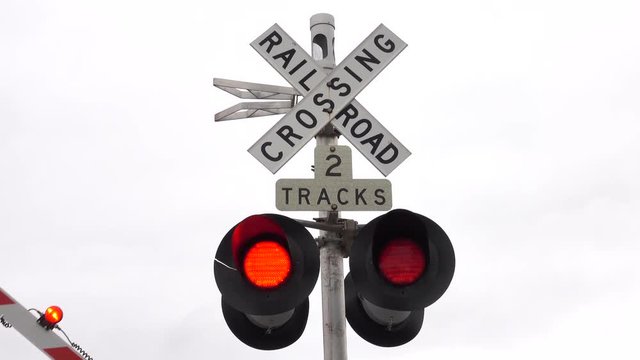 CLOSE UP: Isolated railroad crossing traffic sign with flashing red lights and barrier lowering indicating that a train is coming. Traffic symbols on a intersection of a car road and a railway tracks