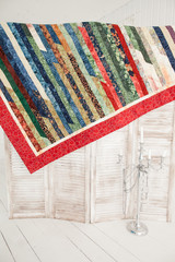 Patchwork quilt hangs on a wooden screen. Part of patchwork quilt in a white room.