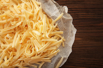 Grated cheese and food paper on wooden background
