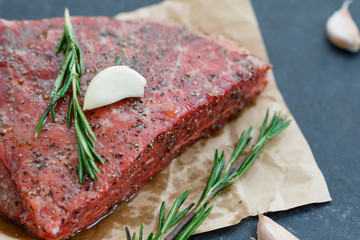 Close-up of raw beef steak on craft paper with garlic and rosemary. Cooking concept. Selective focus.