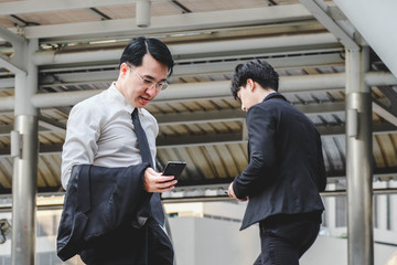 Fototapeta premium Businessman holding and looking smartphone, man walk past
