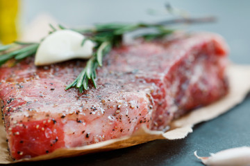 Close-up of raw beef steak on craft paper with garlic and rosemary. Cooking concept. Selective focus.
