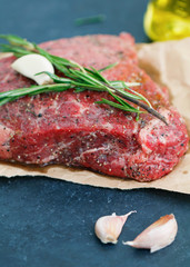 Close-up of raw beef steak on craft paper with garlic and rosemary. Cooking concept. Selective focus.