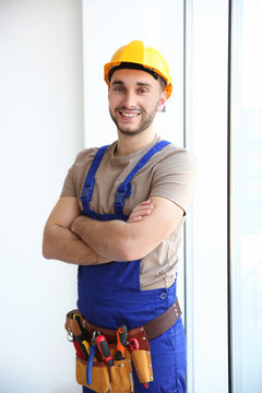 Young smiling electrician standing near big window with crossed hands