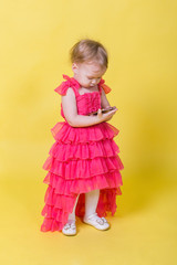 Girl toddler in a pink dress on a yellow background holding a smartphone